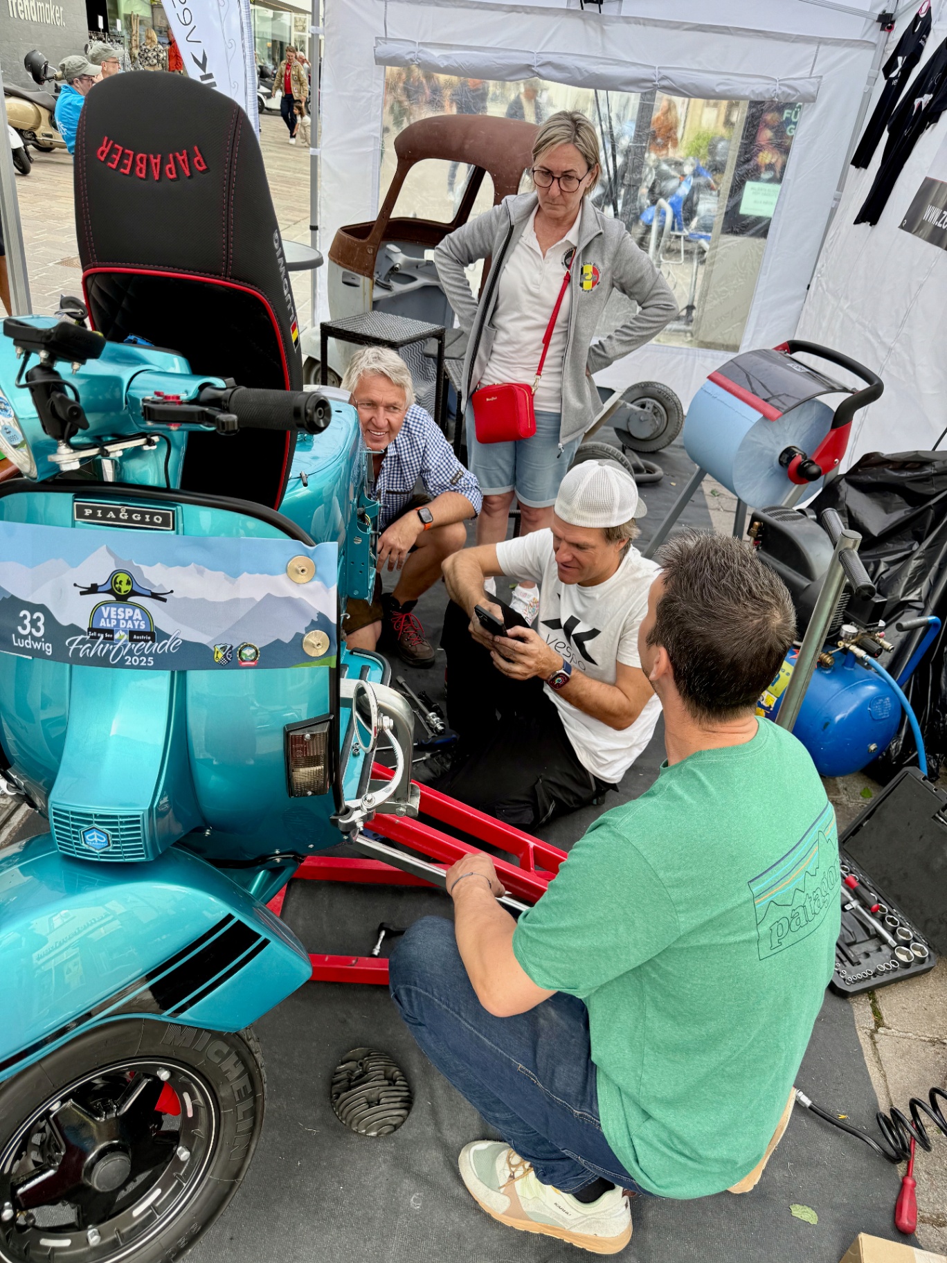 Gerhard repariert eine türkise Vespa, umgeben von Interessierten beim Vespa Alp Days Workshop